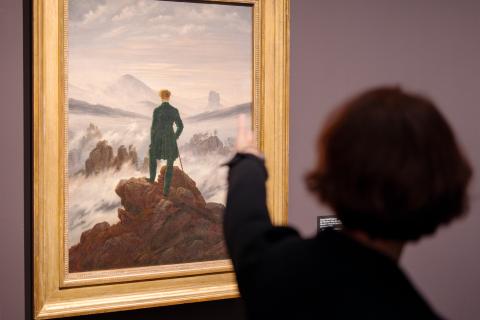 eine Dame von hinten zeigt auf das Gemälde Der Wanderer im Nebelmeer von Caspar David Friedrich
